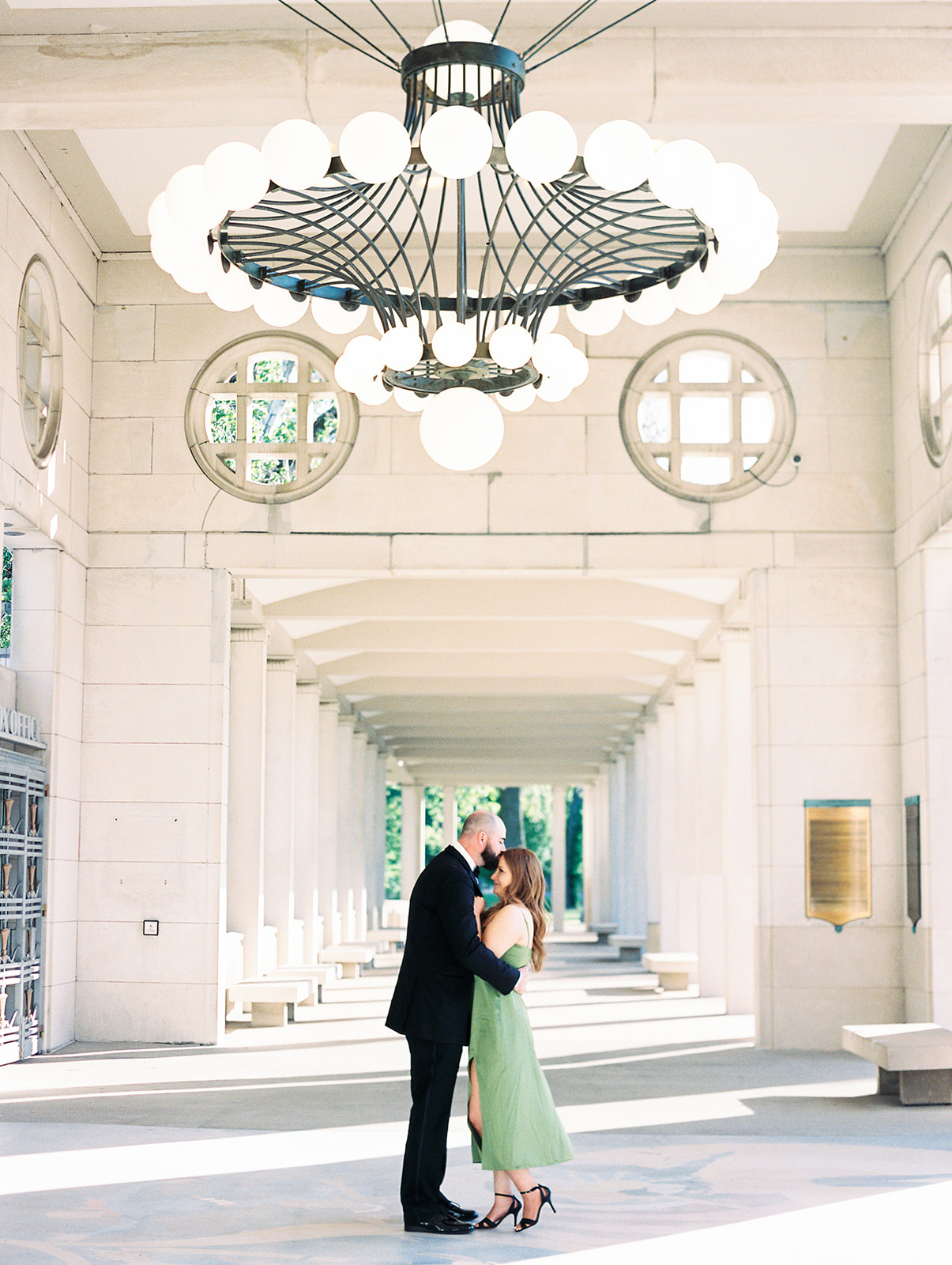 A couple posing for their engagement photos in St. Louis, Missouri at the Muny in Forest Park captured by Kiley Ann Photography. The male subject is wearing a suit jacket and the woman is wearing a green dress.