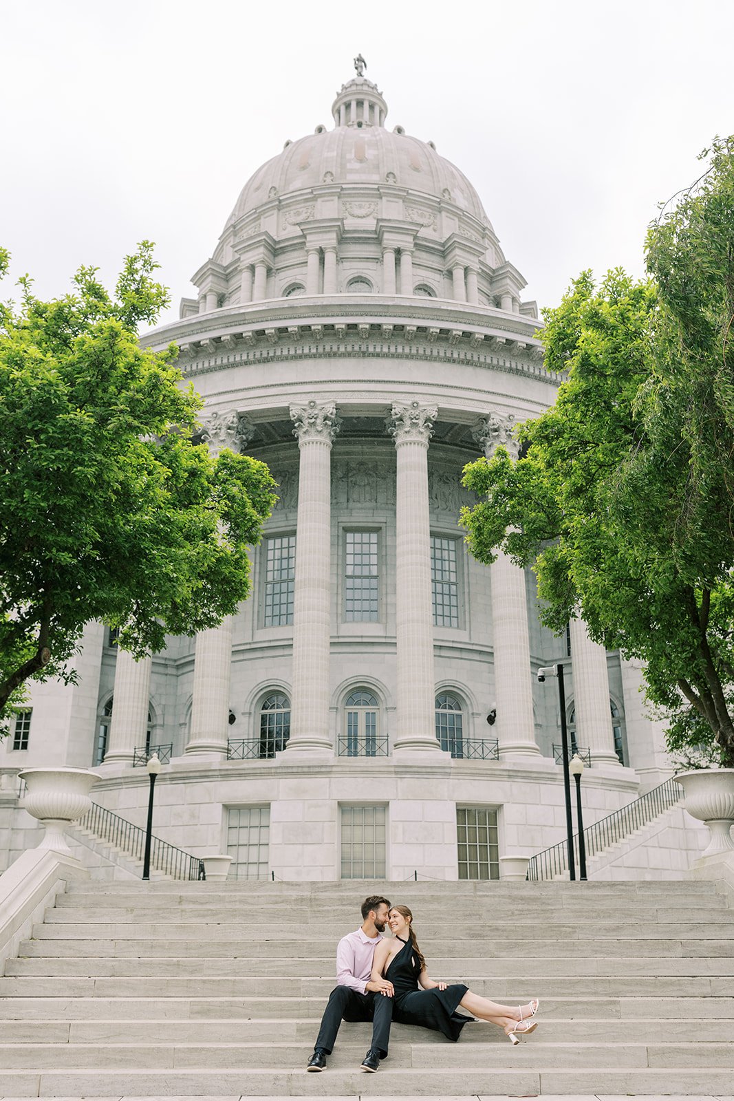 A couple sitting on the steps of the Missouri Capitol during their engagement session in Jefferson City Missouri. They are dressed in classic black attire.