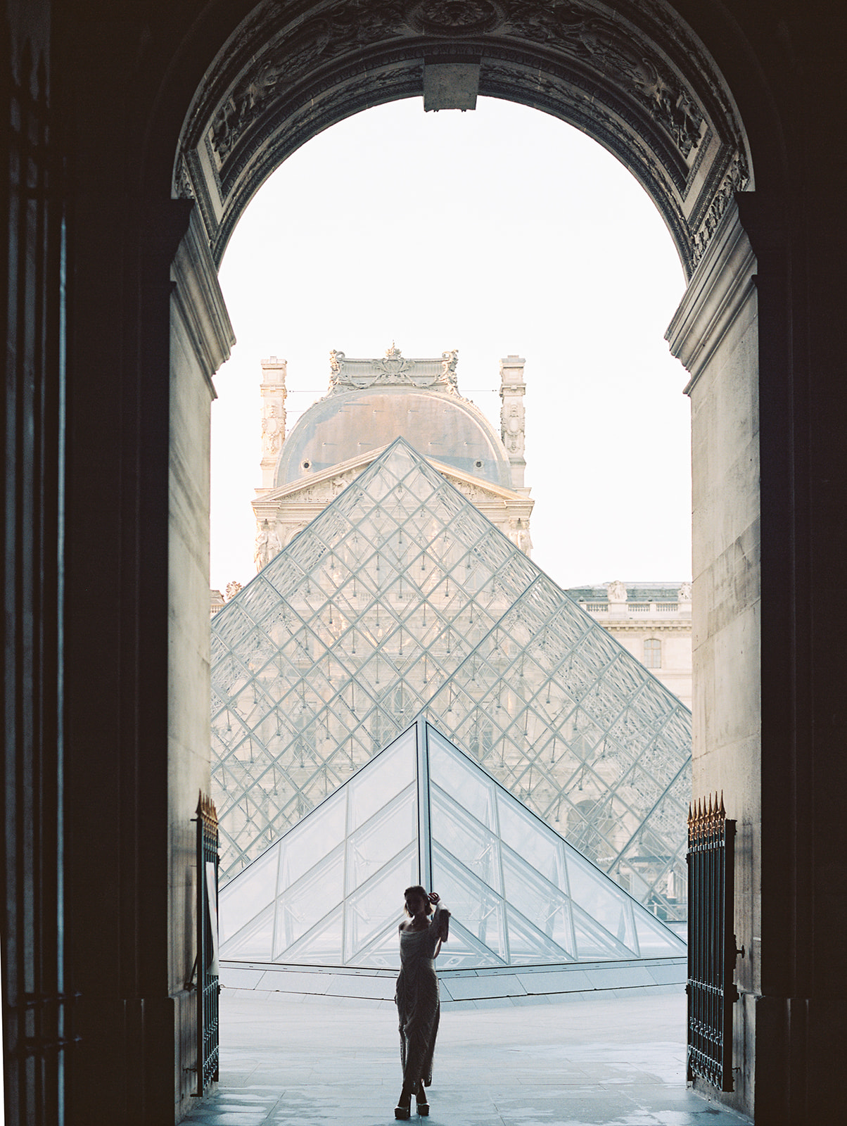A bride standing at the Louvre in Paris, France, as Kiley Ann Photography captures her picture with the pyramid in the background.