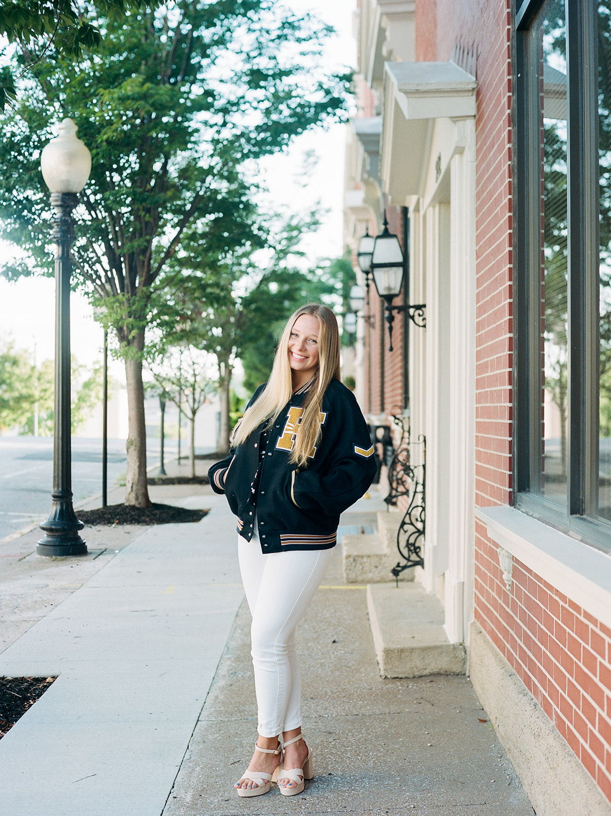 A high school senior standing in her letterman jacket with patches from her sports accomplishments standing in Jefferson City for her portrait session. The photo is captured by Kiley Ann Photography, a photographer based in Columbia, Missouri.