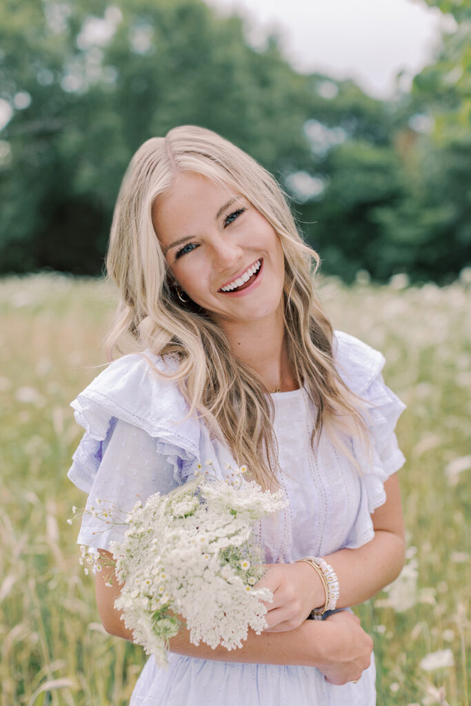 A high school senior wearing a lilac purple dress with puff sleeve posing in a Mid-Missouri field for her summer portrait session with Kiley Ann Photography.