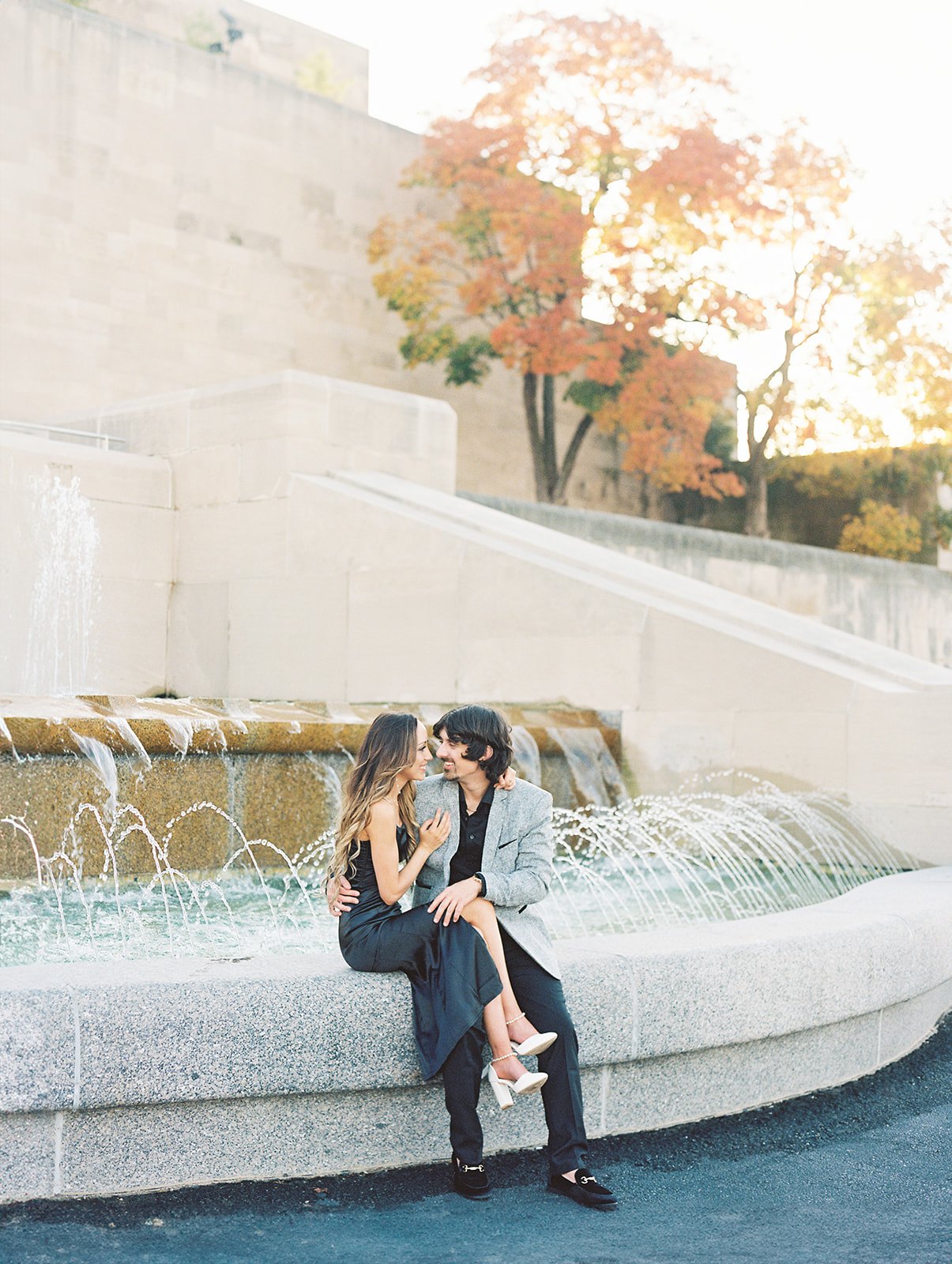 A couple sitting at the Liberty Memorial Tower in Kansas City, Missouri admiring each other by the fountain during their classic themed engagement session photographed by Kiley Ann Photography.